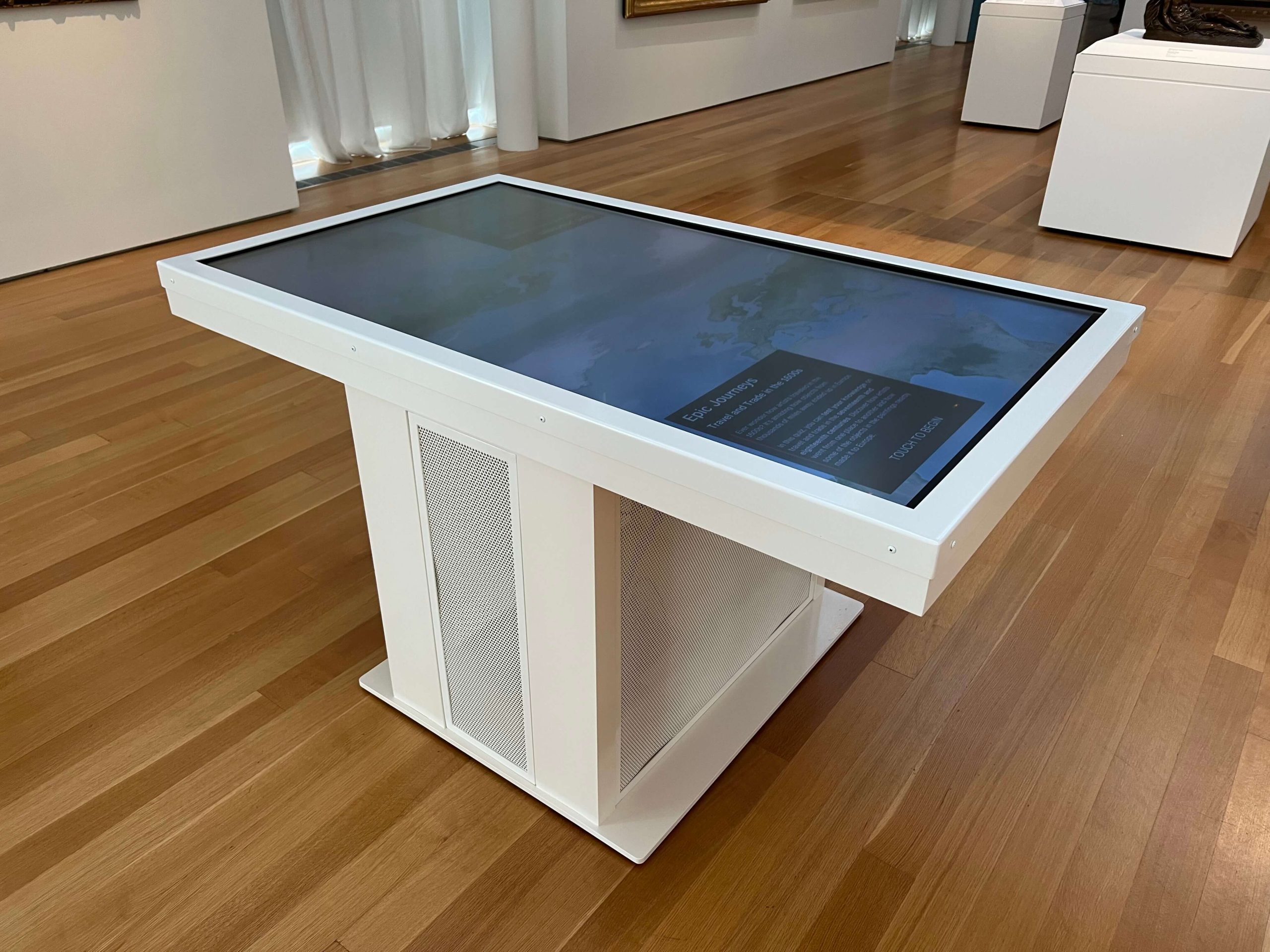 A large touchscreen display is installed horizontally, like a table, in an art museum gallery
